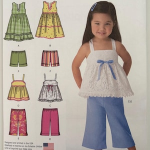 May include: Simplicity sewing pattern 1451 for girls' clothing, featuring various dress and pants designs. The pattern includes a white eyelet top with a blue bow, paired with blue pants. The image also shows a young girl wearing the outfit.
