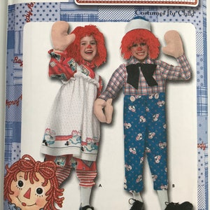 May include: A sewing pattern envelope for Raggedy Ann and Andy costumes for children, size BB 3, 4, 5, 6, 7, 8. The package features illustrations of two children wearing red yarn wigs, white mittens, and outfits with blue, white, and red patterns.