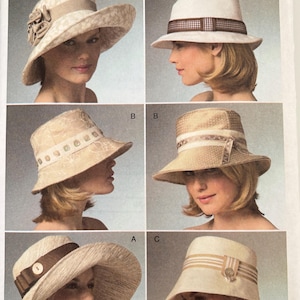 May include: Vogue Accessories pattern V8405 featuring six variations of hats. The designs include wide-brimmed hats and bucket-style hats in shades of cream, beige, and white, accented with ribbons, fabric flowers, buttons, and patterned trim details.