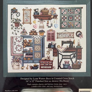 May include: A Dimensions Sew Cozy counted cross stitch kit featuring a detailed pattern of a sewing room with a Singer sewing machine, quilts, and furniture. The package includes charms and buttons, with a finished size of 14 inches by 12 inches.