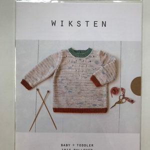 May include: A packaged knitting pattern for a baby and toddler Iris Pullover. The pattern includes a photo of the finished sweater, which is a light-colored knit with brown cuffs and a green collar. The word "WIKSTEN" is printed at the top.