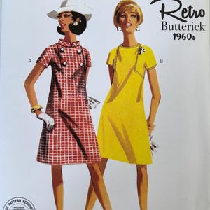May include: Butterick sewing pattern B6990 for two short-sleeved shift dresses. View A is a red and white checkered dress with buttons. View B is a solid yellow dress with decorative trim. The envelope includes size range Y5 18-20-22-24-26.