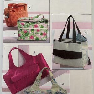 May include: A Vogue Accessories sewing pattern envelope V8098 featuring illustrations of five different bag designs labeled A through E. The bags include various styles such as a floral print rectangular bag, a solid magenta tote, and a city print bag.