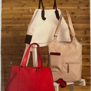 May include: Vogue Accessories sewing pattern V8406 for three tote bags. One bag is white with black handles, one is beige with a front pocket and zipper, and one is solid red. The pattern envelope includes a barcode and the text V8406.
