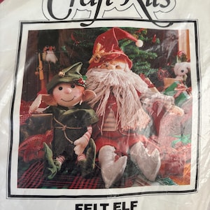 May include: A Better Homes and Gardens Craft Kits package featuring a felt elf and Jingles Santa. The packaging displays a finished elf in a green outfit and a Santa in a red suit with a long white beard, both sitting among wrapped gifts.