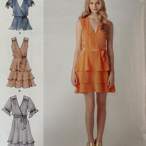 May include: A Simplicity sewing pattern envelope 1872 by Cynthia Rowley featuring three dress variations. The illustrations show a blue short-sleeve wrap dress, an orange sleeveless tiered wrap dress, and a grey short-sleeve tiered wrap dress.