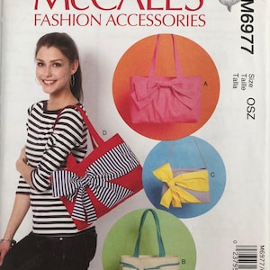 May include: McCall's Fashion Accessories pattern featuring four handbag designs. The bags include a pink tote with a bow, a red tote with a striped bow, a gray clutch with a yellow bow, and a beige tote with a teal bow.