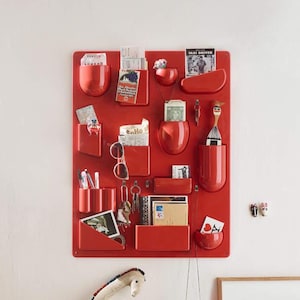 May include: A red wall-mounted organiser with multiple compartments and pockets, holding items such as keys, mail, and pens. A stuffed giraffe and framed artwork are nearby. The organiser is a stylish storage solution.
