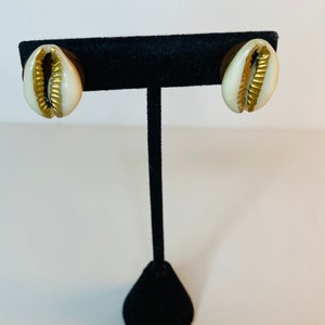 May include: A pair of gold and white shell earrings on a black display stand.