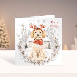 May include: A Christmas card featuring a cute, light brown dog wearing a red scarf and reindeer antlers. The dog is sitting in a snowy winter scene with a small house in the background. The card reads "Merry Christmas".