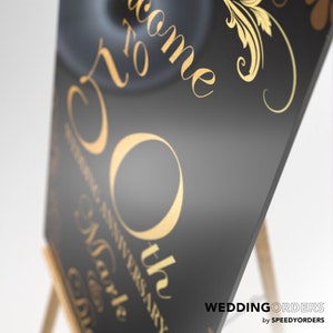 May include: A black rectangular sign featuring gold lettering that reads Welcome to 50th Wedding Anniversary. The design includes elegant gold scrollwork accents and flourishes. The sign is displayed on a wooden easel, presenting a smooth surface.
