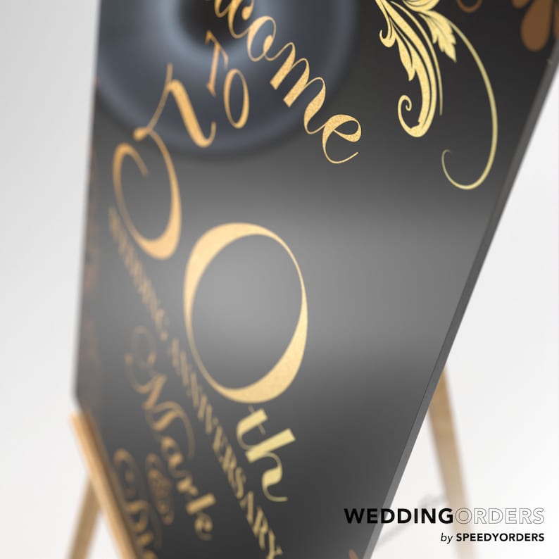 May include: A black rectangular sign featuring gold lettering that reads Welcome to 50th Wedding Anniversary. The design includes elegant gold scrollwork accents and flourishes. The sign is displayed on a wooden easel, presenting a smooth surface.