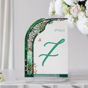 May include: Green and white table number card with a stained glass arch design and a green butterfly. The card says "Table 7" in a green cursive font.
