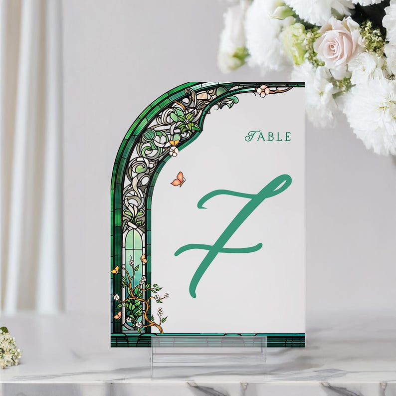 May include: Green and white table number card with a stained glass arch design and a green butterfly. The card says "Table 7" in a green cursive font.