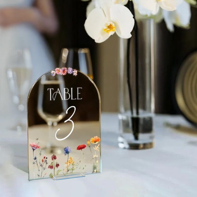 May include: A mirrored table number card with a floral design and the text "TABLE 3" in white lettering.