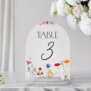 May include: White table number card with a floral design. The card is shaped like an arch and has the text "TABLE 3" printed on it.