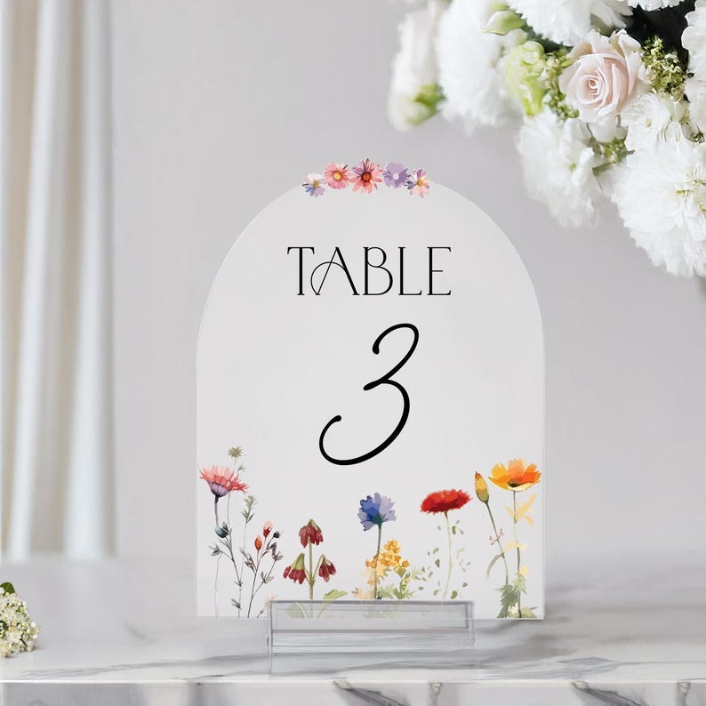 May include: White table number card with a floral design. The card is shaped like an arch and has the text "TABLE 3" printed on it.