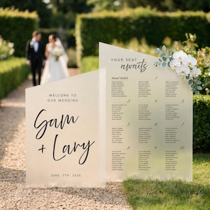 May include: A wedding seating chart with the words "Welcome to Our Wedding" and the names "Gam + Lary" and the date "June 7th 2026". The chart also includes the words "Your Seat Awaits" and a list of names. White orchids and greenery decorate the top.