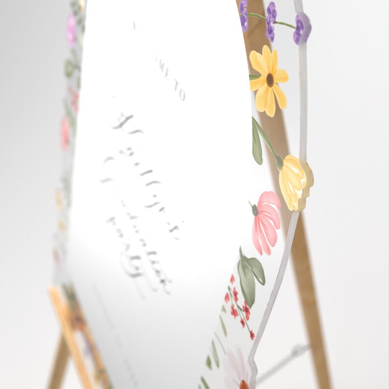 May include: A hexagonal clear acrylic sign featuring a floral border with yellow, pink, and purple flowers and green leaves. The sign displays text in a script font, including the words Welcome to, and is mounted on a light-colored wooden easel stand.