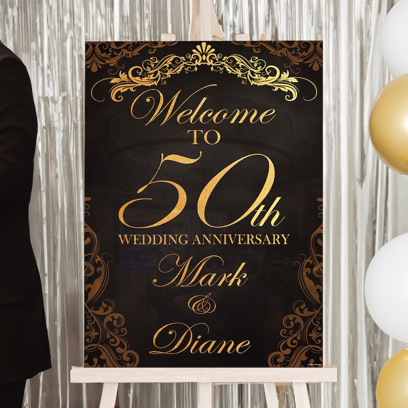 May include: A rectangular sign with a black background and gold decorative filigree borders. The text reads Welcome TO 50th WEDDING ANNIVERSARY Mark & Diane in gold lettering. The sign is displayed on a wooden easel stand for event decor.