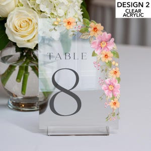 May include: Clear acrylic table number with floral design. The number 8 is displayed in a dark gray font. The top right corner has a floral design with pink and orange flowers. The text "DESIGN 2 CLEAR ACRYLIC" is in the top right corner.