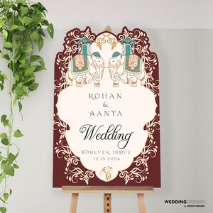 May include: A rectangular wedding sign with a maroon border and ornate white filigree. It features two illustrated elephants with teal and gold saddles at the top. The text reads: ROHAN & AANYA, Wedding, FOREVER IN LOVE, and 12.15.2024.
