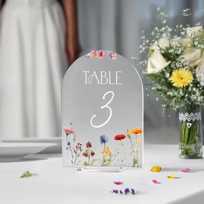 May include: A clear acrylic table number with a floral design and the text "TABLE 3" in white lettering.