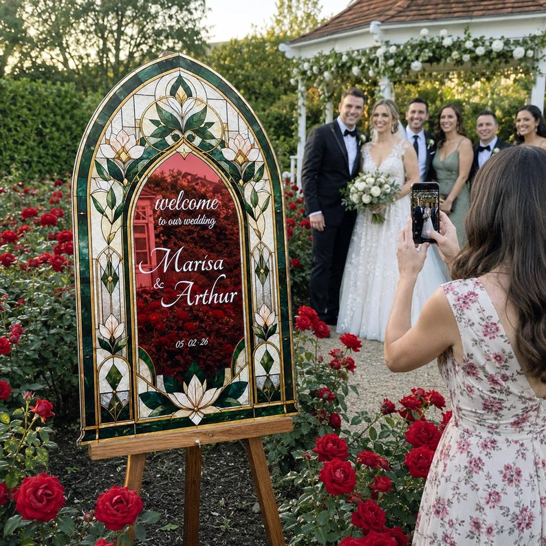 May include: An arched wedding welcome sign featuring a stained glass border with green and white floral patterns. The center panel displays the text "welcome to our wedding", "Marisa & Arthur", and the date "05-02-26" in white script lettering.