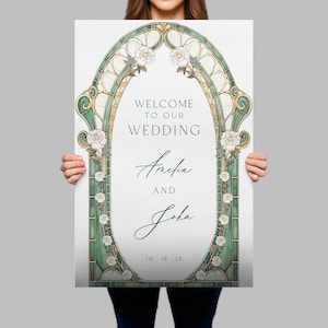 May include: A rectangular wedding welcome sign featuring an oval frame with green stained glass patterns and white rose illustrations. The text reads: WELCOME TO OUR WEDDING, Amelia AND John, 10 . 15 . 25. The design uses dark green and gold accents.