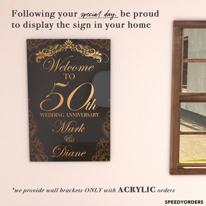 May include: A rectangular black acrylic sign featuring gold decorative scrollwork borders and gold text that reads Welcome to 50th Wedding Anniversary Mark & Diane. The sign is displayed on a wall next to a wooden window frame.