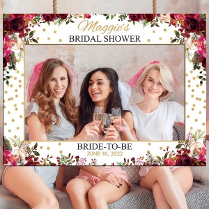 May include: A white photo booth frame with a gold and burgundy floral design. The frame has the text "Maggie's Bridal Shower" and "Bride-to-Be June 30, 2022".