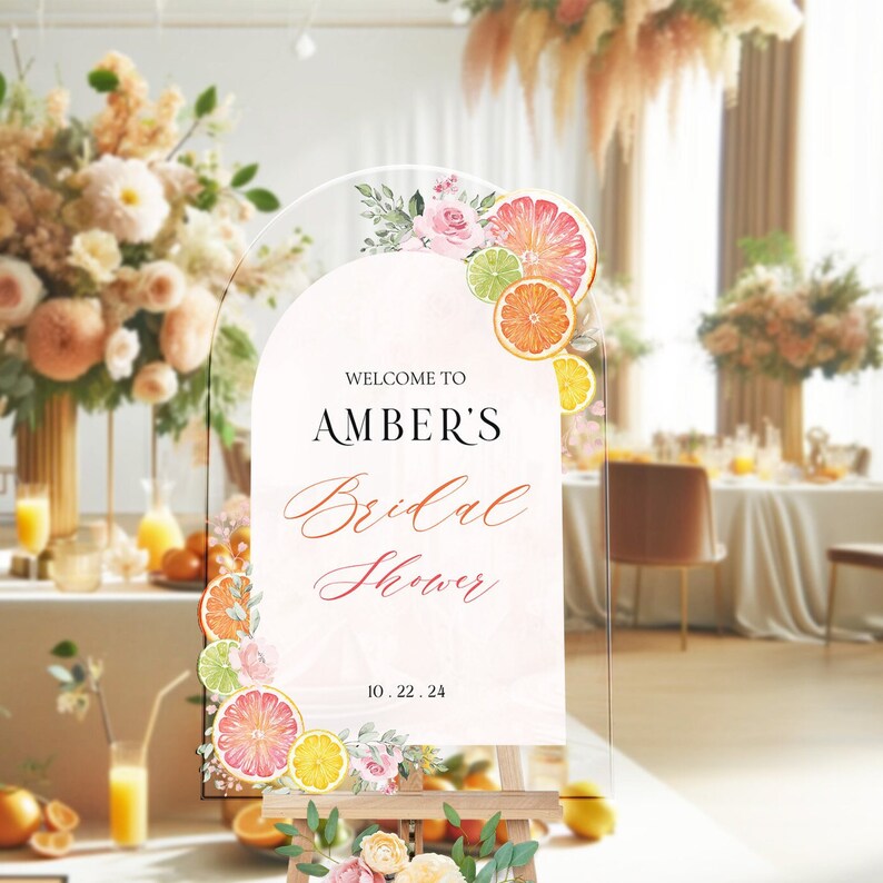 May include: A welcome sign for a bridal shower with a citrus theme. The sign is made of clear acrylic and features a watercolour illustration of lemons, limes, and oranges with pink flowers. The text on the sign reads "Welcome to Amber's Bridal Shower 10.22.24".