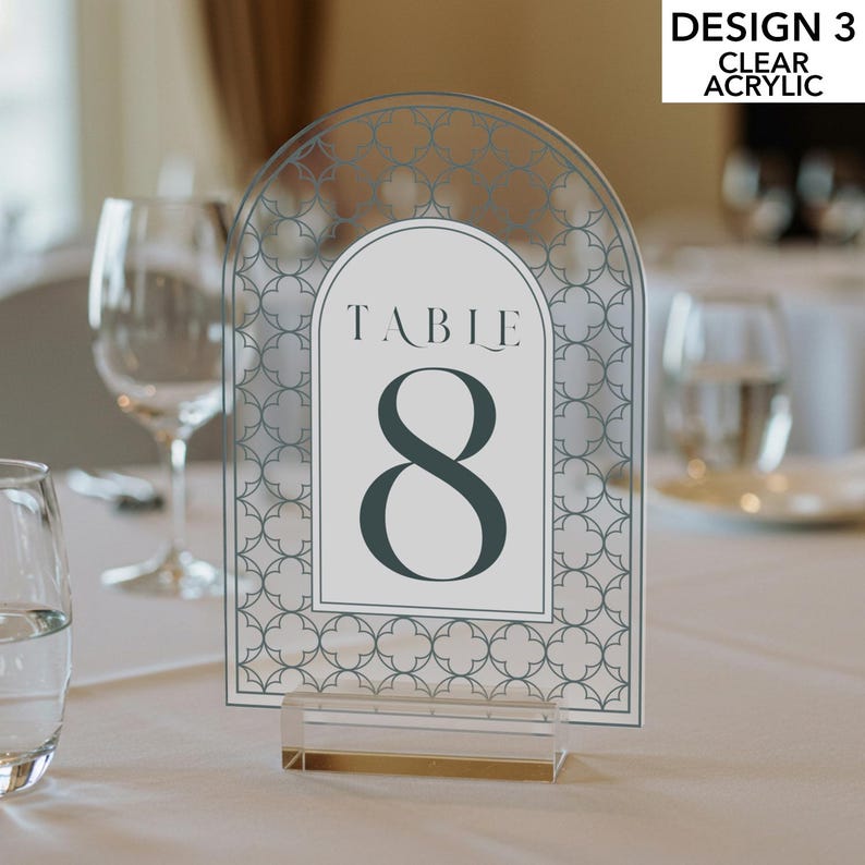 May include: Clear acrylic table number with a decorative geometric pattern. The design features the number 8 in a dark teal color, with the word "TABLE" above it. The text "DESIGN 3 CLEAR ACRYLIC" is in the upper right corner. The table number is held by a clear acrylic base.