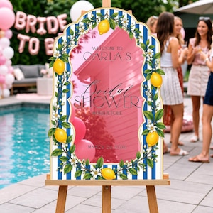 May include: An arched welcome sign for a bridal shower featuring a blue and white vertical striped border decorated with yellow lemons and white blossoms. The center text reads: Welcome to Carla's Bridal Shower #bridetobe March 04 2026.
