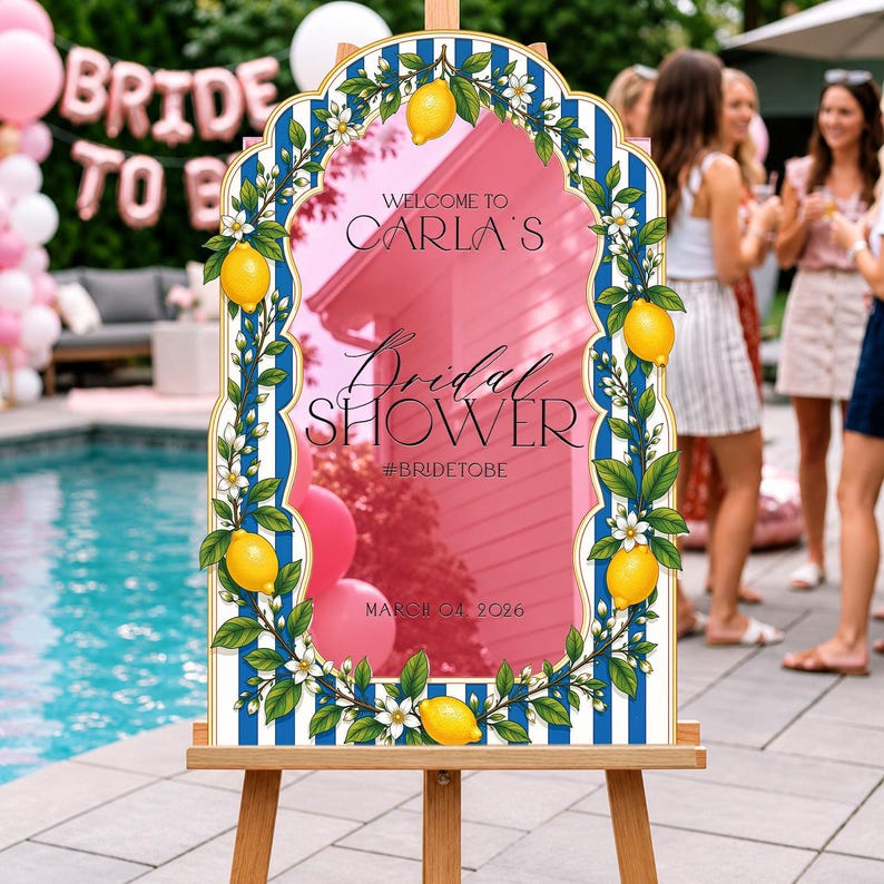 May include: An arched welcome sign for a bridal shower featuring a blue and white vertical striped border decorated with yellow lemons and white blossoms. The center text reads: Welcome to Carla's Bridal Shower #bridetobe March 04 2026.