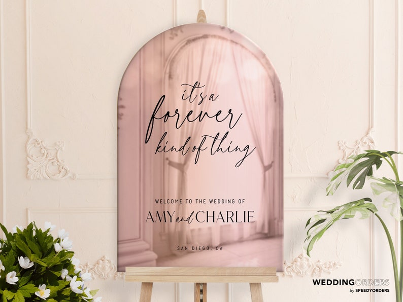 Może przedstawiać: Łukowata tablica powitalna na ślub w odcieniu delikatnego r&oacute;żowego złota z czarnym napisem "it's a forever kind of thing", "WELCOME TO THE WEDDING OF AMY and CHARLIE" oraz "SAN DIEGO, CA", umieszczona na drewnianej sztaludze.