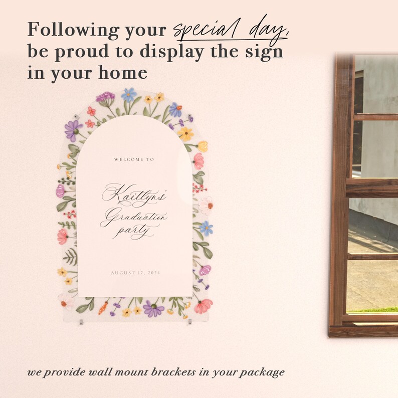 May include: An arched acrylic sign featuring a colorful floral border with purple, blue, yellow, and pink flowers. The text reads: Welcome to Kaitlyn's Graduation party, August 17, 2024. The sign is mounted with silver hardware on a light wall.