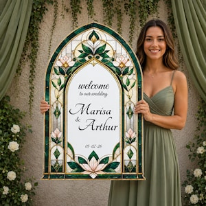 May include: An arched wedding welcome sign featuring a stained glass-style border with dark green and light pink floral patterns. The center white panel displays the text: welcome to our wedding, Marisa & Arthur, and the date 05-02-26.