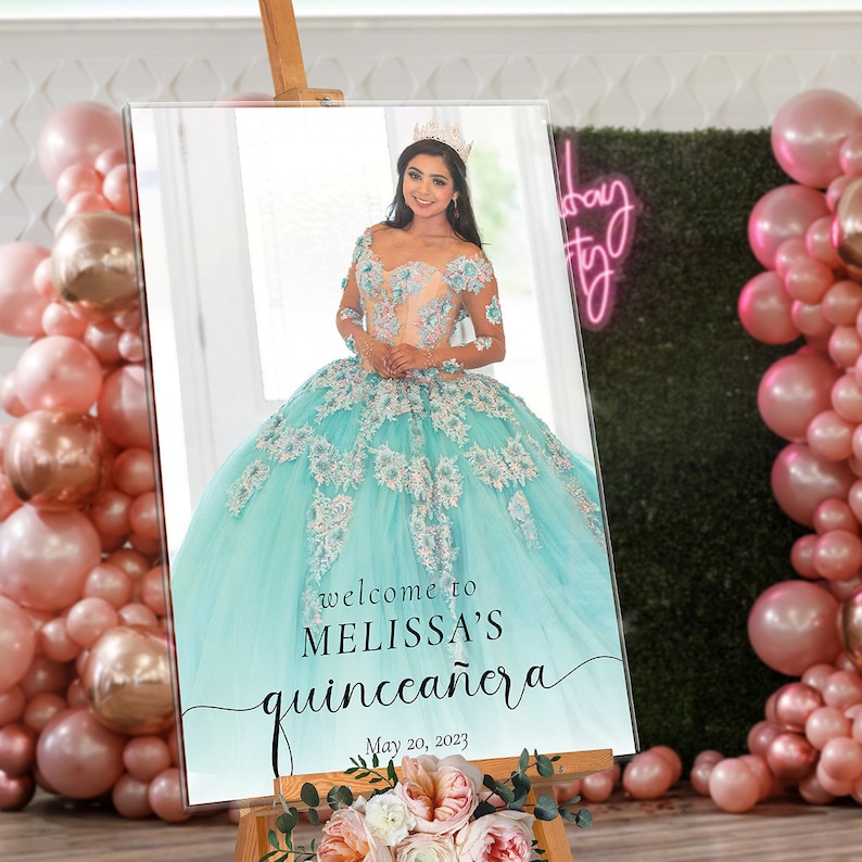 May include: A welcome sign for a quincea&ntilde;era celebration. The sign features a photo of a young woman in a light blue and white dress with a crown on her head. The text on the sign reads "Welcome to Melissa's Quincea&ntilde;era" and "May 20, 2023".