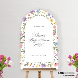 May include: An arched white welcome sign for a baby shower featuring watercolor floral illustrations along the border. The text reads Welcome to Becca's Baby Shower party October 22, 2024. The sign is displayed on a wooden easel with bouquets of tulips.