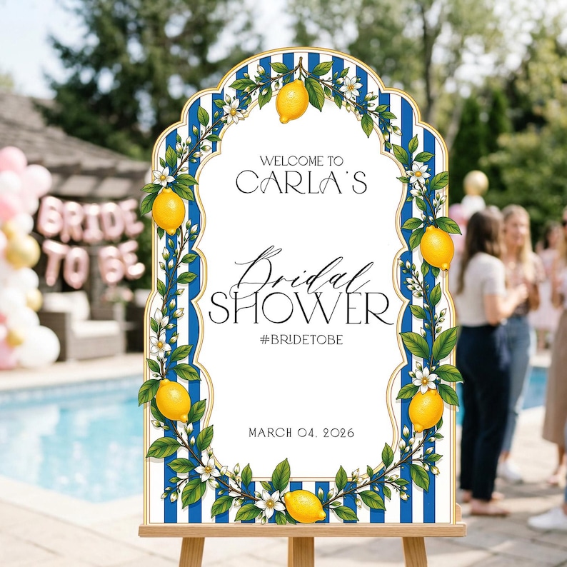 May include: An arched sign with a blue and white vertical striped border featuring illustrations of yellow lemons and white blossoms. The text reads: WELCOME TO CARLA'S Bridal SHOWER #BRIDETOBE MARCH 04, 2026. The sign is displayed on a wooden easel.