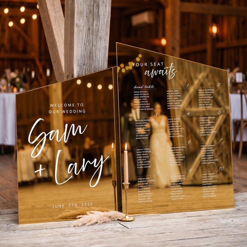 K&ouml;nnte beinhalten: Zwei goldfarbene, abgewinkelte Hochzeitsschilder. Auf einem Schild steht "Willkommen zu unserer Hochzeit" und "Gam + Lary, 7. Juni 2026". Das andere Schild listet die Namen der G&auml;ste und Tischnummern auf. Ein Kerzenhalter mit zwei Kerzen steht davor.