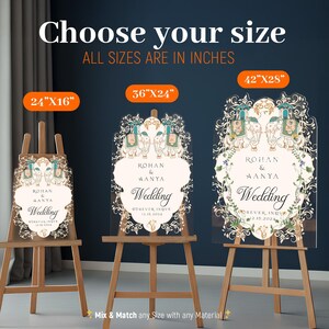 May include: Three clear acrylic wedding signs on wooden easels, labeled 24x16 inches, 36x24 inches, and 42x28 inches. Each sign features an ornate border with two elephants, floral motifs, and the text Rohan & Aanya Wedding Forever Inove 12.15.2024.