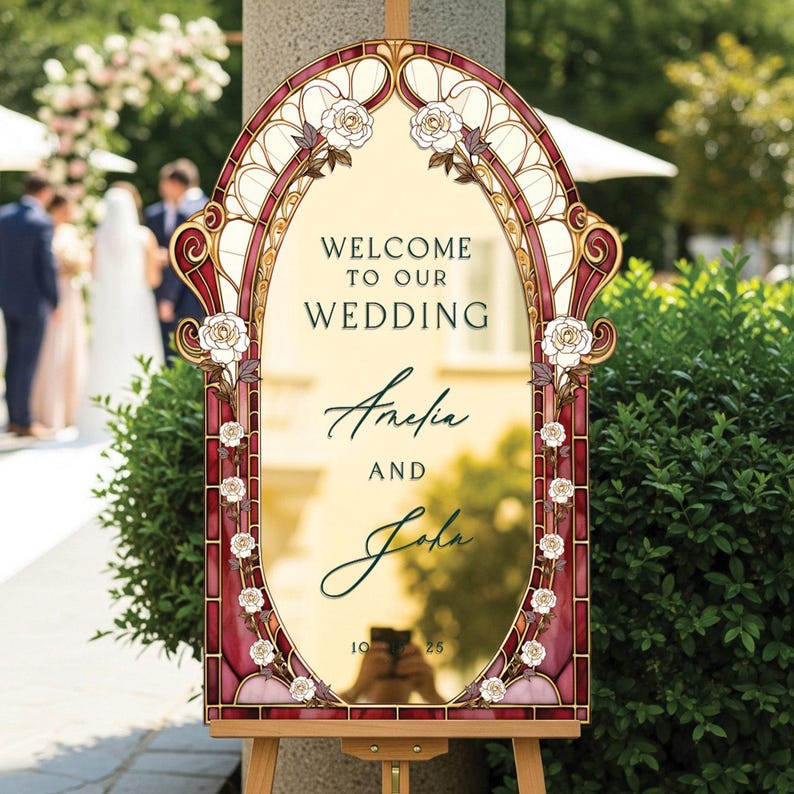 May include: A decorative wedding sign with a stained-glass design. The sign reads "Welcome to our Wedding" above the names "Amelia and John" and the date "10.25". The sign is framed with burgundy and gold accents and white roses.