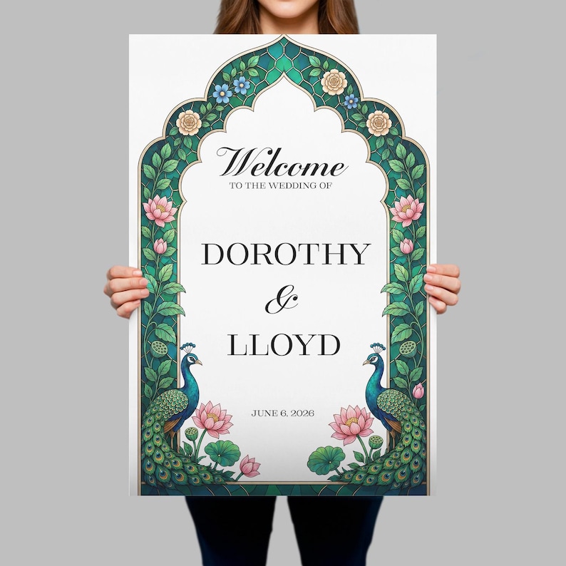 Op de afbeelding: Een rechthoekig welkomstbord voor een bruiloft met een boogvormige rand versierd met groene bladeren, blauwe en cr&egrave;mekleurige bloemen en roze lotusbloemen. Twee pauwen met blauwe halzen en groene staarten flankeren de tekst: Welcome to the wedding of Dorothy & Lloyd, June 6, 2026.