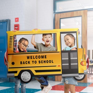 May include: Three children pose for a photo holding a yellow cardboard cutout of a school bus. The bus has the words "Welcome Back to School" printed on the front.