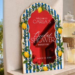 May include: An arched sign with a blue and white striped border decorated with yellow lemons and white blossoms. The red center features white text: WELCOME TO CARLA'S, Bridal SHOWER, #BRIDETOBE, and MARCH 04, 2026. The sign has a gold-toned trim.