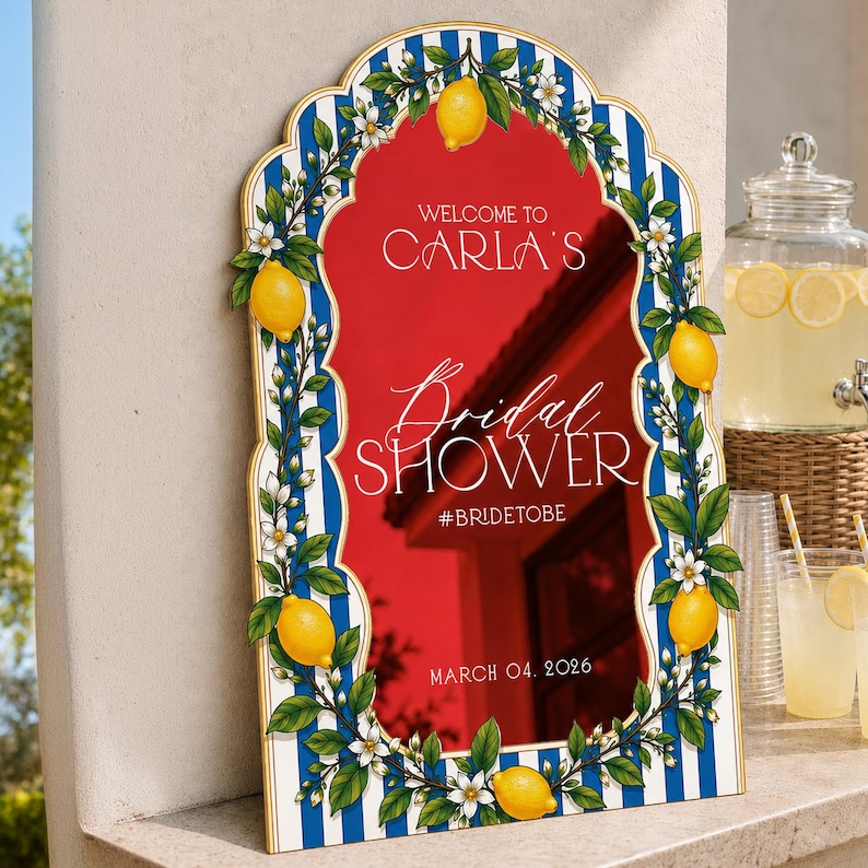 May include: An arched sign with a blue and white striped border decorated with yellow lemons and white blossoms. The red center features white text: WELCOME TO CARLA'S, Bridal SHOWER, #BRIDETOBE, and MARCH 04, 2026. The sign has a gold-toned trim.