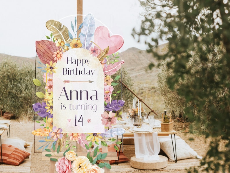 May include: An arched acrylic birthday sign featuring watercolor illustrations of flowers, feathers, and a heart. The text reads Happy Birthday, Anna is turning 14, with a small arrow graphic. The sign is displayed on a wooden easel stand.