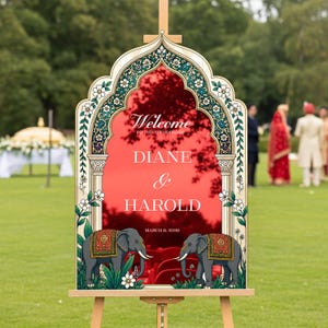 Peut inclure: Un panneau de bienvenue de mariage avec un fond rouge en forme d'arche et le texte blanc Welcome to the wedding of Diane & Harold March 6, 2026. Le cadre est orn&eacute; de motifs floraux et de deux &eacute;l&eacute;phants gris avec des couvertures rouges.